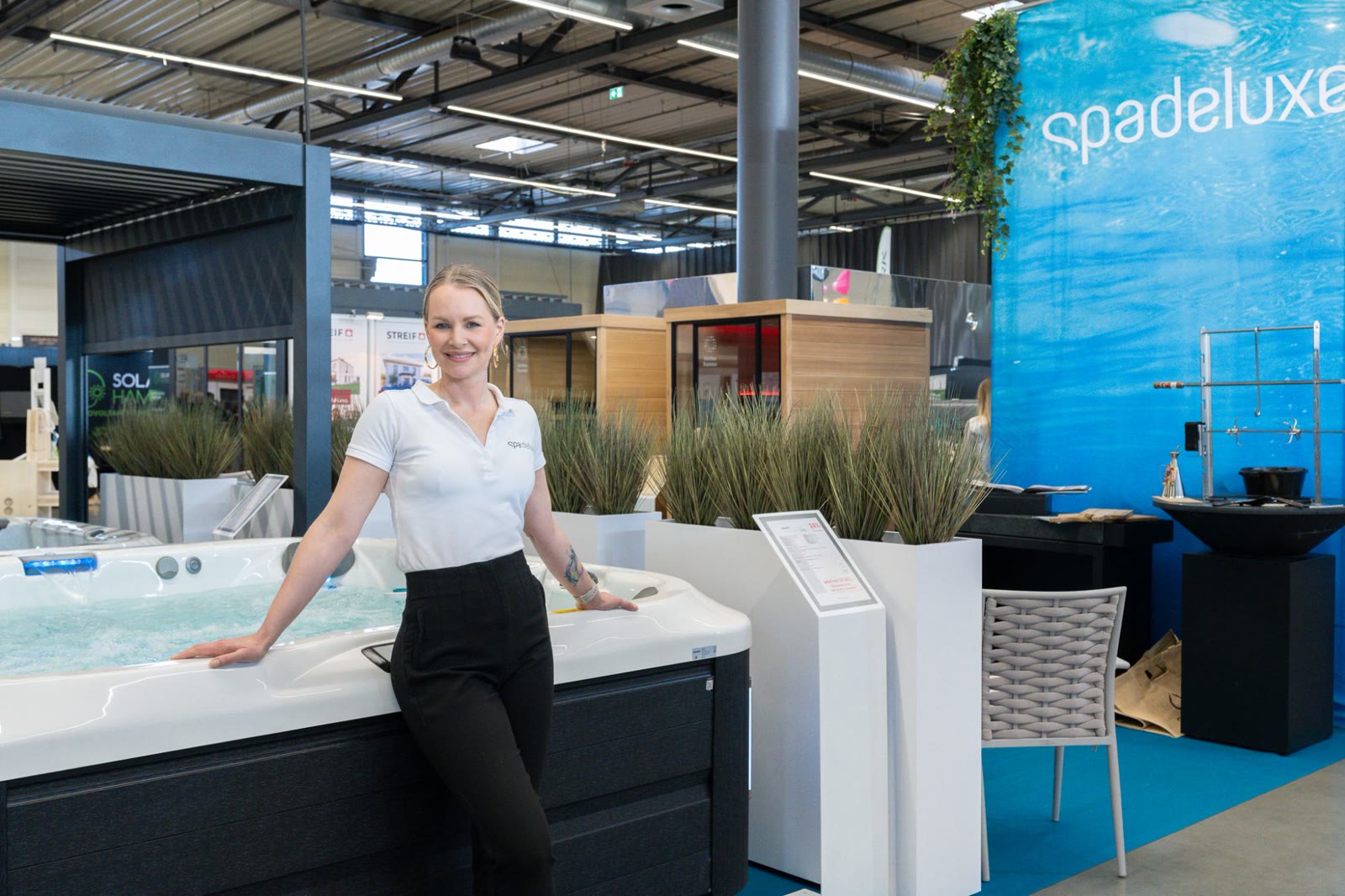 Beraterin von SPA Deluxe lehnt am Messestand an einem befüllten Whirlpool
